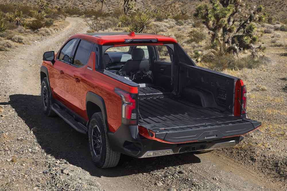Rear 3/4 view of the 2026 Silverado EV Trail Boss in Habanero Orange, showcasing the open Midgate pass through.